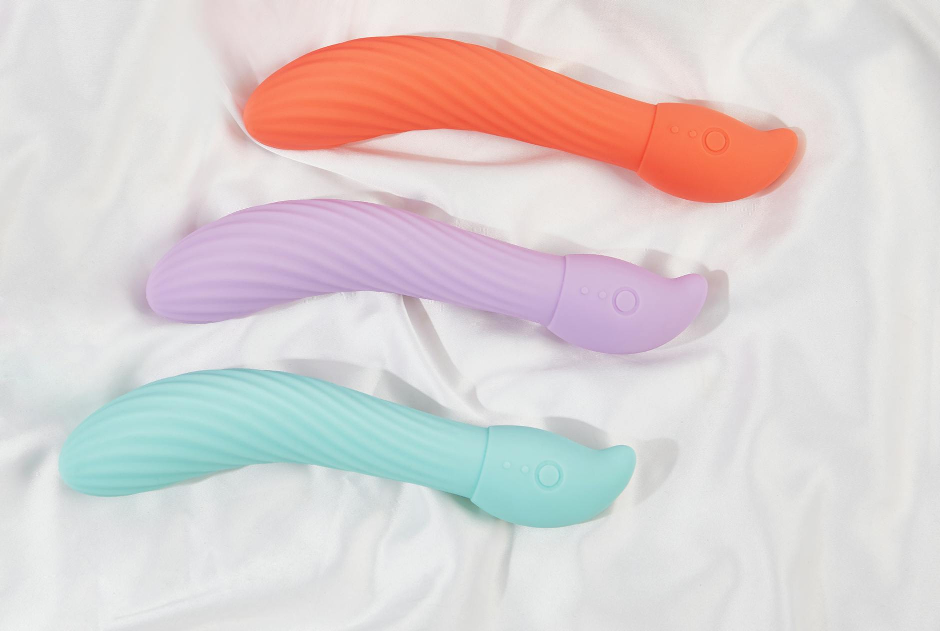 Woman holding blue and pink silicone vibrators in a contemplative manner