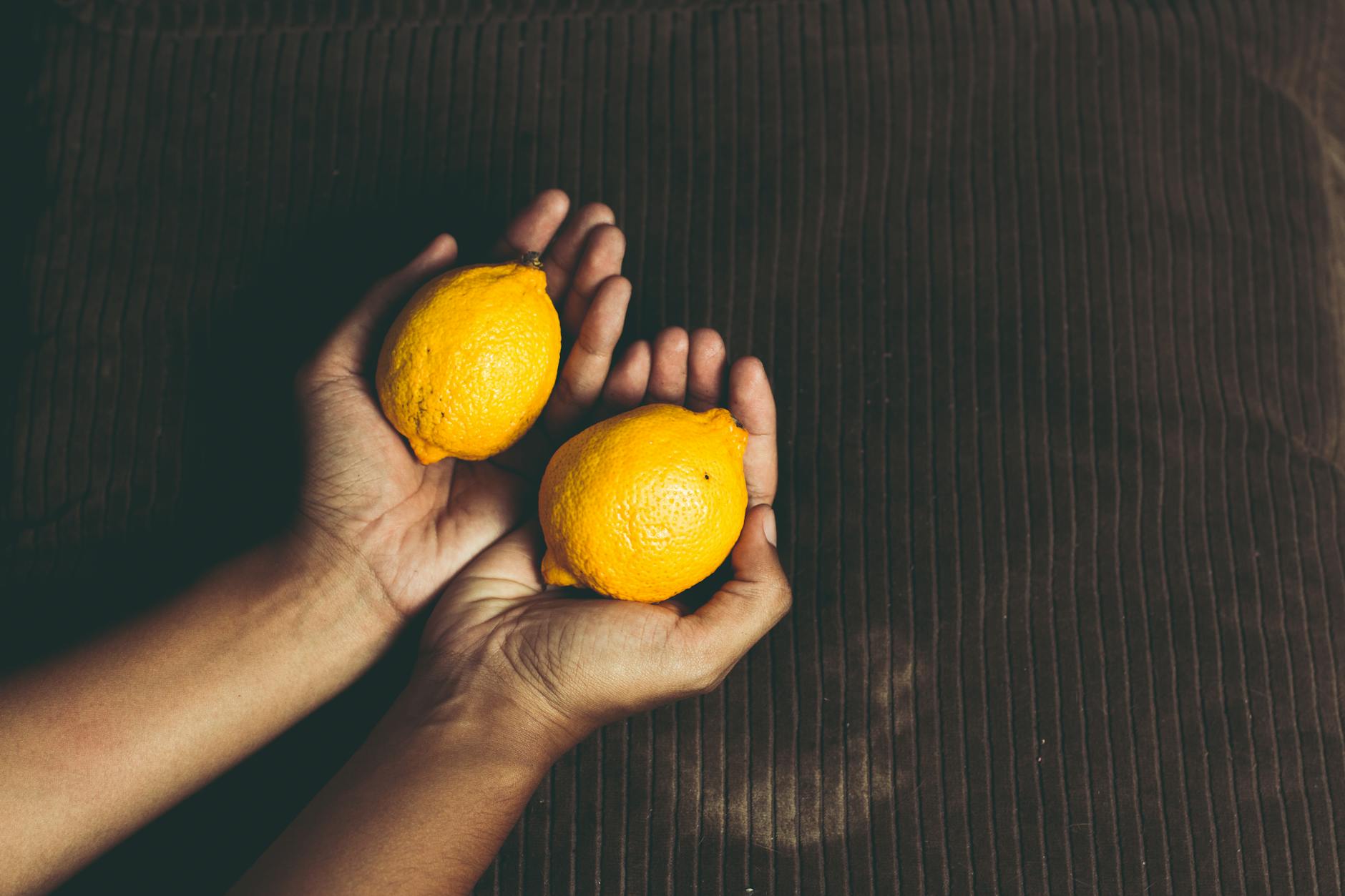 Close-up of two fresh lemons held in cupped hands, symbolizing the gentle touch approach to pleasure after pelvic tension