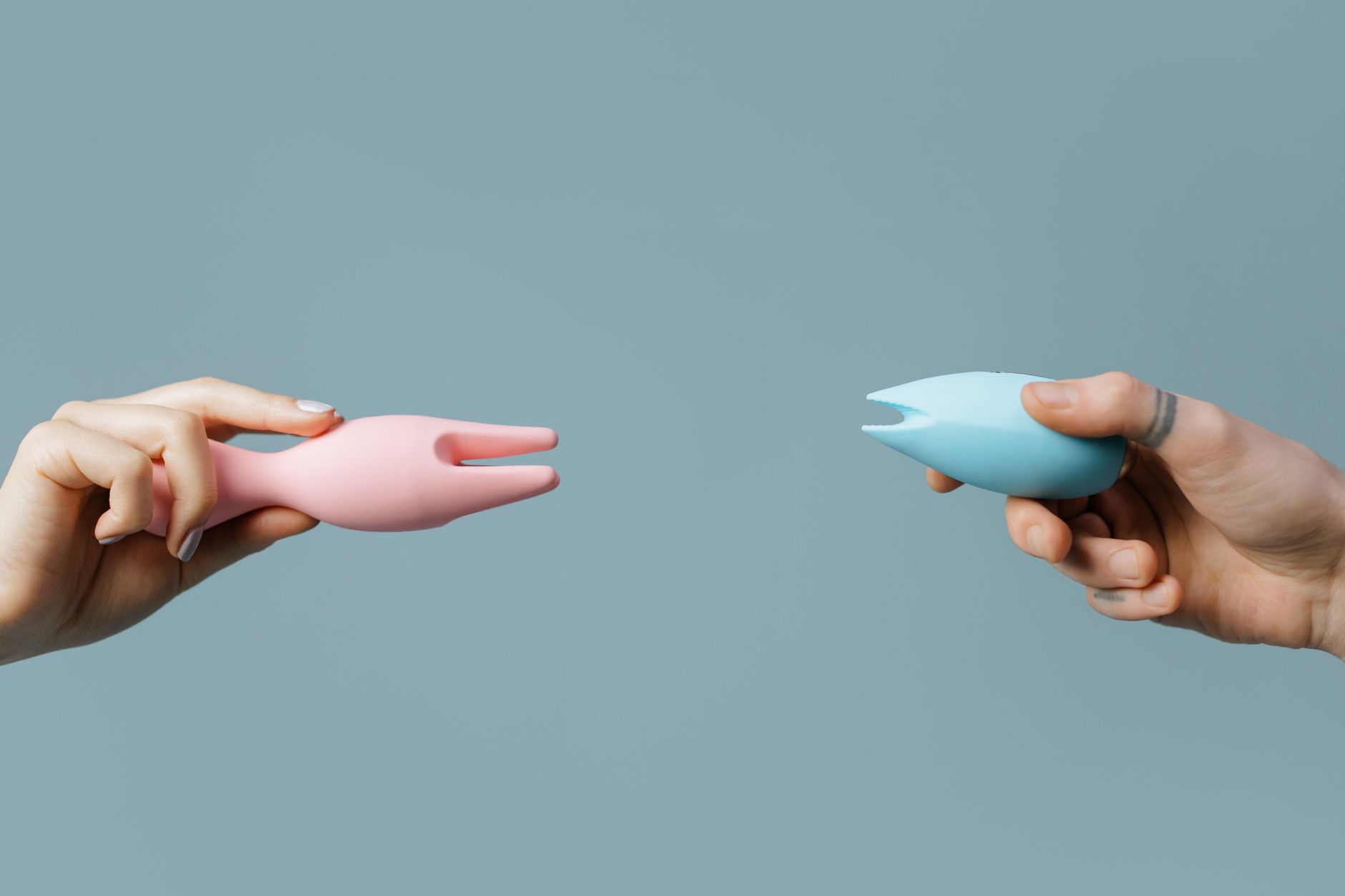 Two hands holding vibrators against a pastel background, symbolizing partnership and shared pleasure exploration.