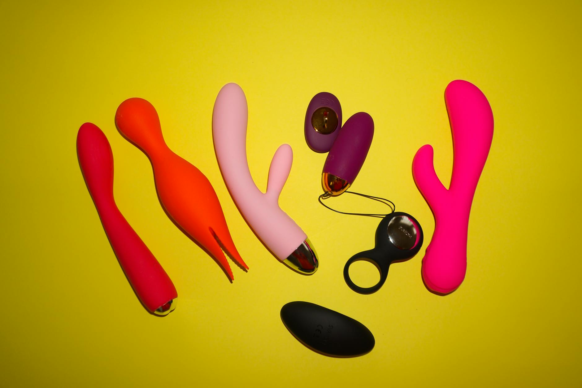 Colorful sex toys on a bright yellow background, featuring various shapes and designs