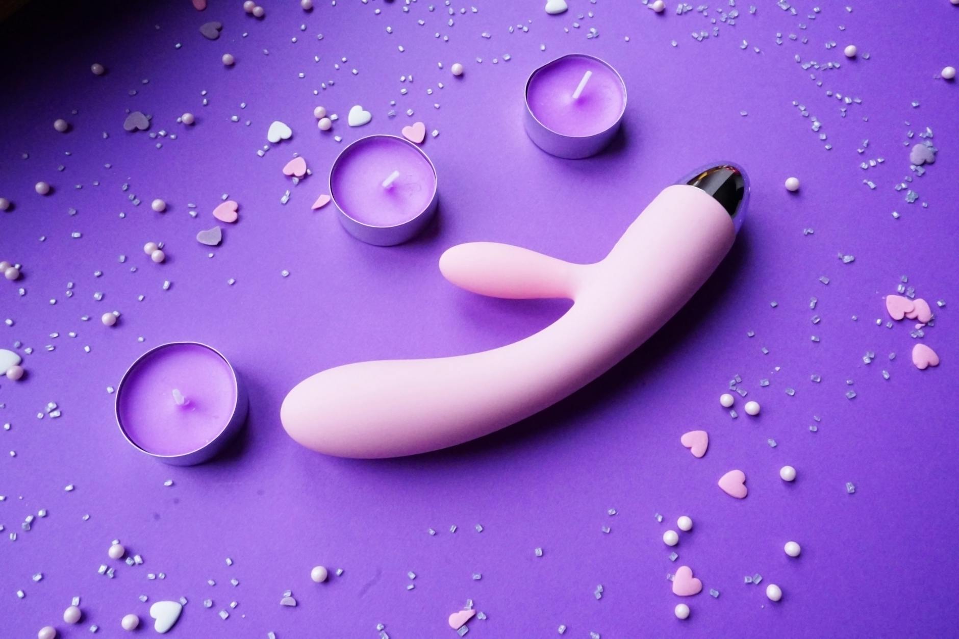 A hand holding an orange vibrator against a purple backdrop